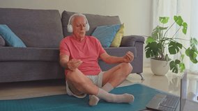 Senior man wearing headphones meditating in living room while following online tutorial on laptop - Powered by Shutterstock - Get 15% off with code: PIKWIZARD15