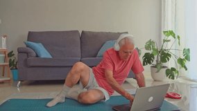 Elderly man wearing headphones on yoga mat using laptop for online workout in living room - Powered by Shutterstock - Get 15% off with code: PIKWIZARD15