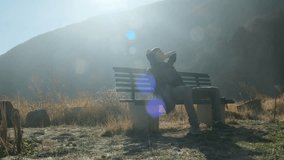 A lone young man rests on a bench in the mountains, leaning back with his hands behind his head and eyes closed, enjoying nature and silence. Relaxing outdoors in a national park. A happy young guy - Powered by Shutterstock - Get 15% off with code: PIKWIZARD15