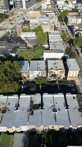 Circular drone pan above Jersey City blocks showing rooftop variations, spaced buildings, and connected streets in afternoon clarity.