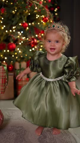 Cute little child in festive dress and crown smiling near Christmas tree. New Year celebration concept.