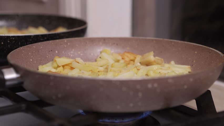 Potatoes cut into slices are deliciously fried in a frying pan.