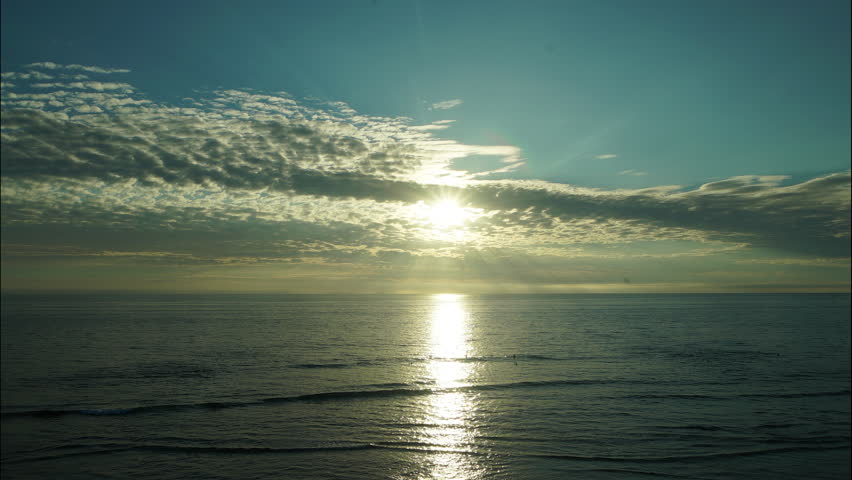 Timelapse of a glowing sunset over the Pacific Ocean horizon with surfers.