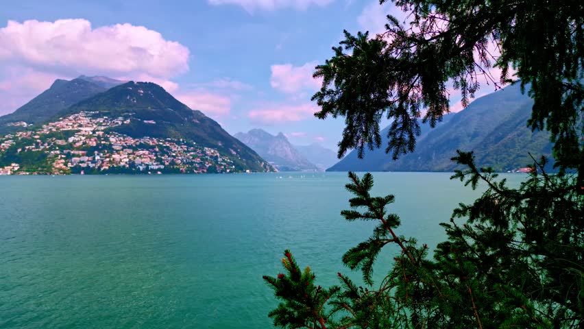 Lugano, Switzerland – September 5, 2023: View across Lake Lugano toward Monte Brè and the Italian Alps with a small boat in the frame, seen through branches.