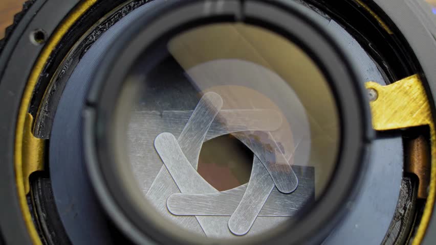 Shot of Diaphragm blades of fixed camera lens opening and closing aperture. Closing and opening Aperture of film camera. Camera lens aperture close-up.