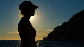 Silhouette of a woman kissing the sun at sunset over the sea. Side profile silhouette of a woman in a cap standing on a boat and looking at the ocean during a golden sunset, with sun flares - Powered by Shutterstock - Get 15% off with code: PIKWIZARD15