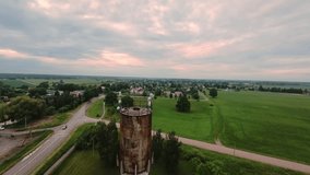 aerial rusty water tower over fields at sunset with pastel clouds, winding road, small village, lush green farmland, weathered metal texture, tranquil cinematic dusk atmosphere, slow drone - Powered by Shutterstock - Get 15% off with code: PIKWIZARD15
