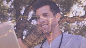 Male doctor tapping tablet under tree reviewing patient data as network graphic growing over frame. Stethoscope, scrubs, healthcare, telehealth, digital, analytics, visualization - Powered by Shutterstock - Get 15% off with code: PIKWIZARD15