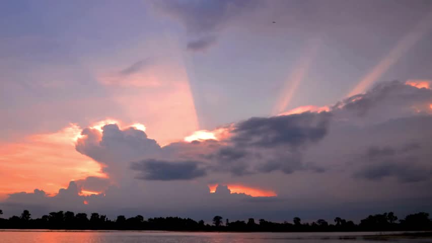 Dramatic sunset over a calm lake with colorful clouds and sun rays shining through