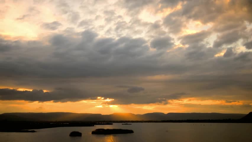 Golden sunset over a tranquil lake with mountains and dramatic cloudy sky view