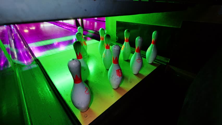 Green-lit bowling lane from rare angle shows dramatic impact and remaining pins