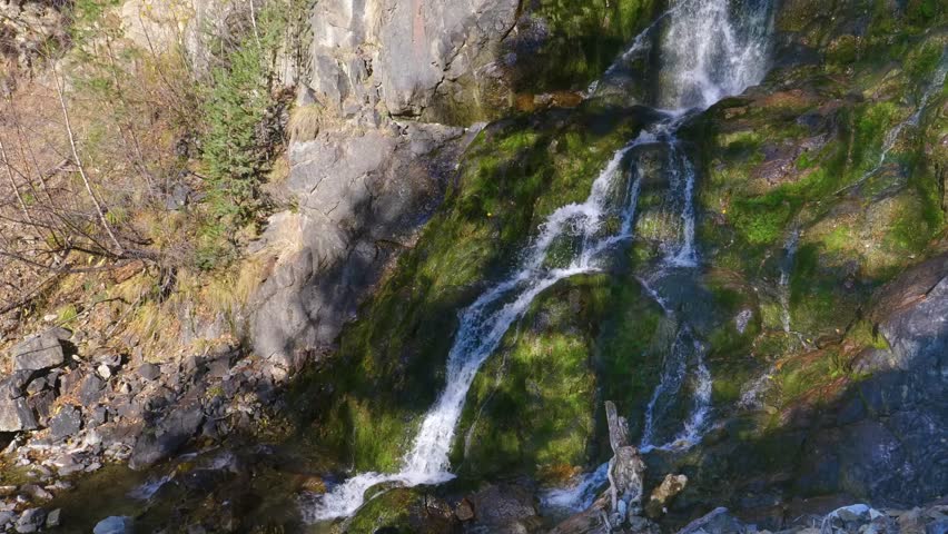 A view of a waterfall cascading down a moss covered rocky cliff in the scenic mountains of the North Caucasus region, Russia.