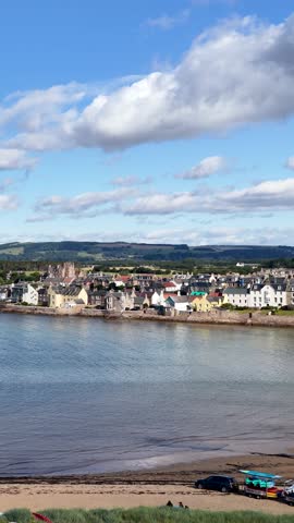 Smooth aerial pan reveals colorful waterfront village, calm harbor, and scenic landscape under bright daylight