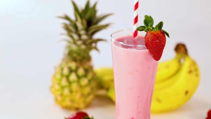 Tall glass of pink smoothie with strawberry, banana, pineapple, and berries, bright studio lighting