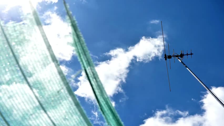 Antenna reaches for the sky under a bright blue sky with a sunlit green tarp nearby