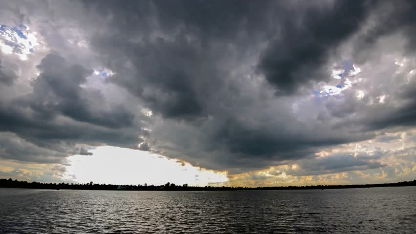 Ominous storm clouds gather over a serene lake landscape at dusk creating drama