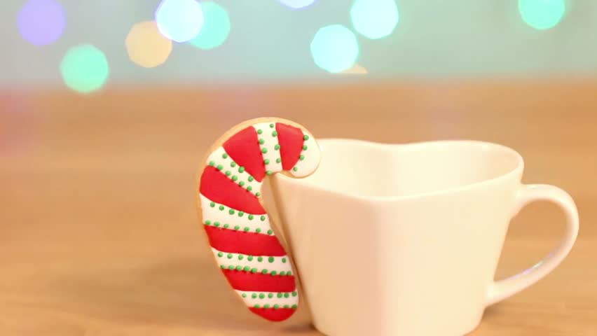 Festive candy cane cookie hanging on a white heart shaped mug with bokeh lights