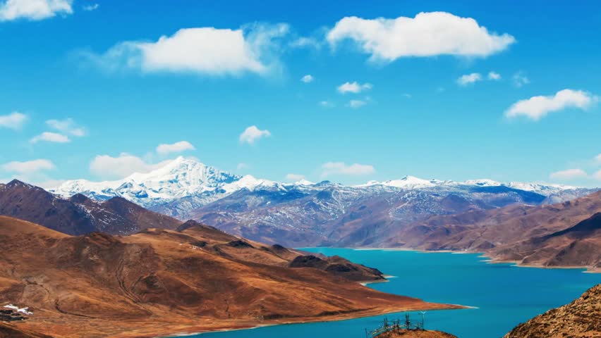 Serene turquoise lake nestled among brown mountains under a bright blue sky day
