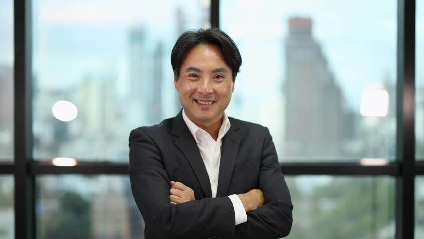 Businessman in suit stands, crosses arms, and smiles in bright, contemporary office setting