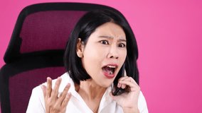 Asian woman in white shirt expresses surprise and concern on phone, seated against pink background - Powered by Shutterstock - Get 15% off with code: PIKWIZARD15