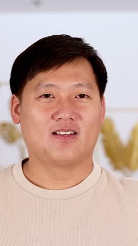 Confident Asian man in beige shirt flexes arm, showing strength and determination indoors.