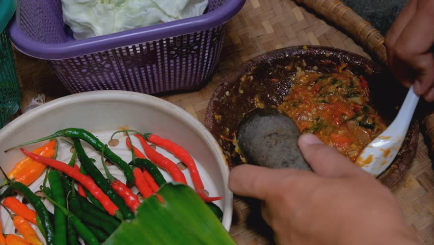 A traditional Indonesian sambal terasi being made with a stone mortar and pestle, featuring freshly ground chilies, tomatoes, and shrimp