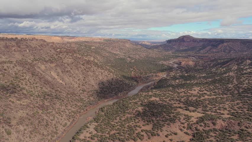 A broad aerial view of the Rio Grande flowing through wide canyon slopes framed by distant mesas and layered desert hills.