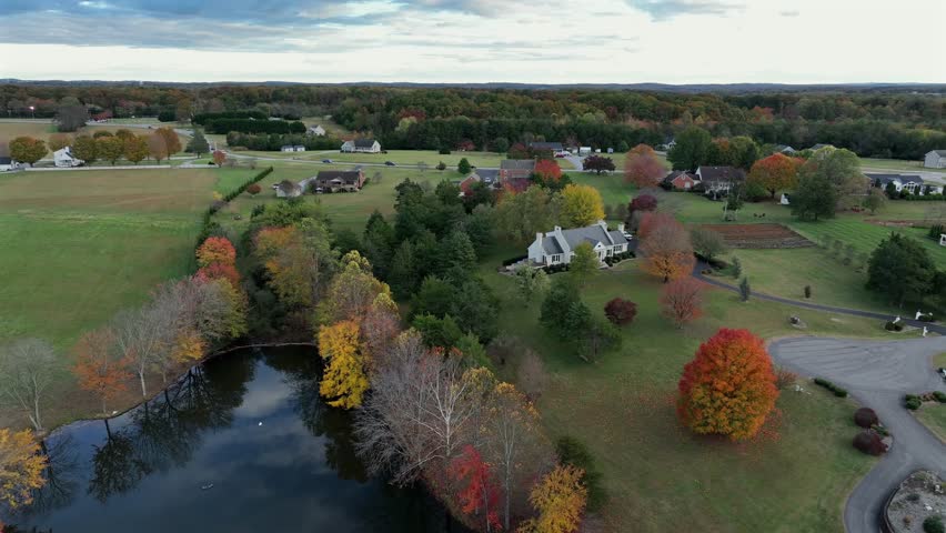 Mansion with private lake and colored trees in fall season. Quiet suburbia of american town. Aerial wide shot. Cul-de-sac in neighborhood.