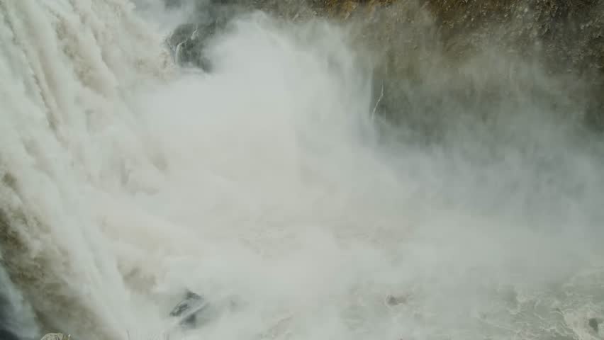A close up shot of a powerful waterfall in Iceland, showing a large volume of white, foamy water rushing over rocks and boulders. The dynamic movement of the water creates a sense of raw, untamed natu