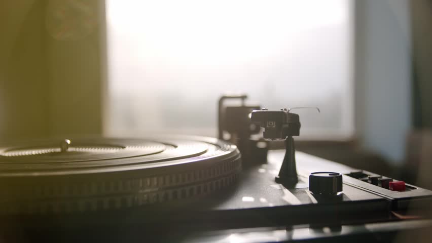 Close-up of a hand turning a vintage vinyl record in sunlight, capturing nostalgic music vibes, warm indoor lighting, and retro atmosphere.