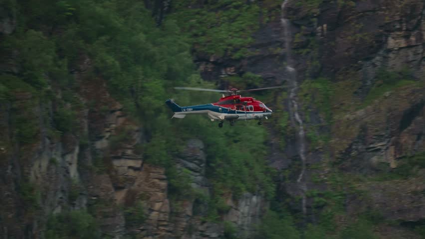 Helicopter flies near steep cliffs in Geiranger Fjord, Norway. Rescue mission