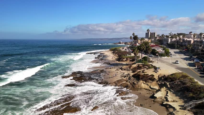 A smooth coastal flyover showing La Jolla’s sandy beach, clear waves, and bright California scenery.