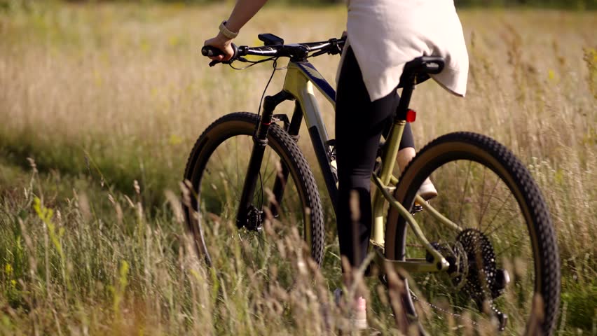 Riding Mountain Bike Through Sunny Field. Female Cyclist On Off-Road Trail. Summer Outdoor Sport Activity Fitness Training In Nature, Endurance Cycling. Fitness Journey Sports Equipment. Active Living