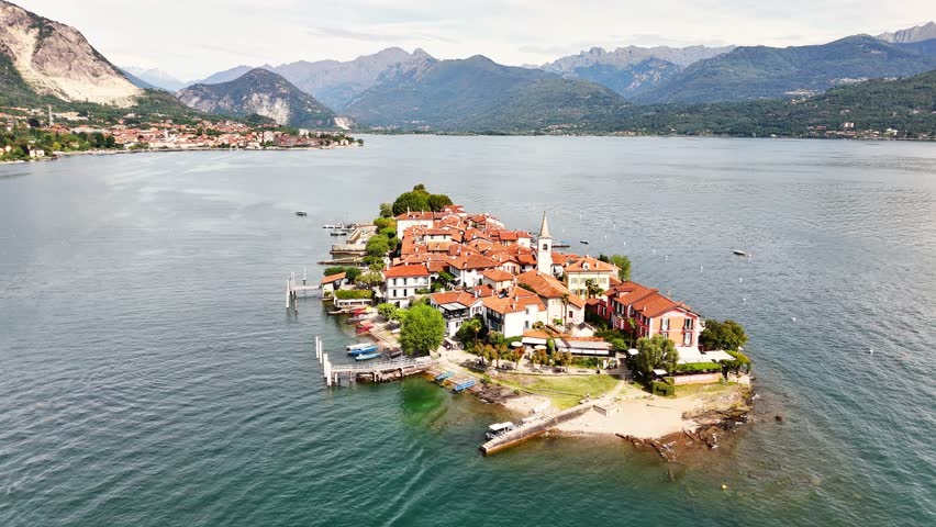 A tranquil view of Sresa on Isola Bella in Italy featuring a compact lakeside village with red roofs, gentle water, small boats, and distant mountain ranges forming a peaceful and scenic landscape