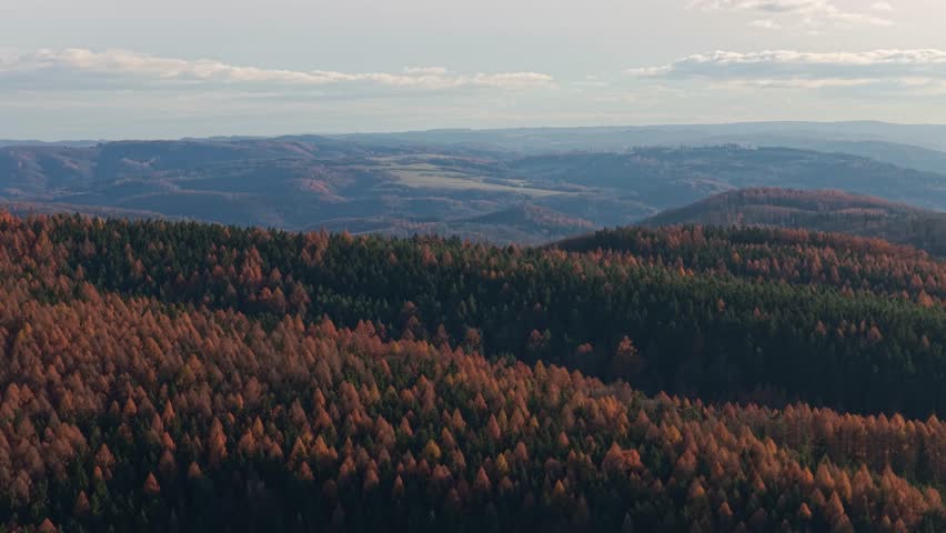 Aerial view of wooded hills with beautiful autumn colors. Rural landscape with clouds in the background.