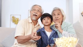 Grandparents and grandson laughing together, sharing popcorn while watching a movie in cozy living room. - Powered by Shutterstock - Get 15% off with code: PIKWIZARD15