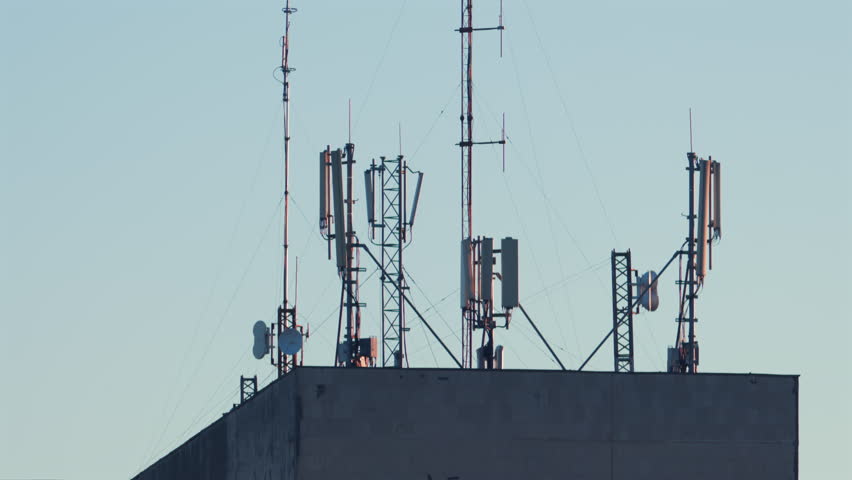 Antennas and communication towers stand on top of a building under the warm morning light