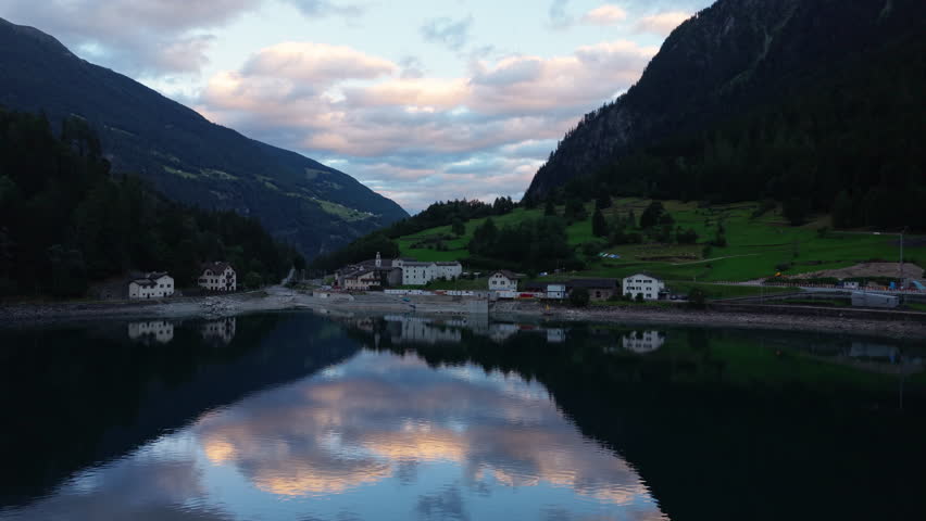 Lakeshore Village At The Foot Of The Mountains At Sunrise In Switzerland. Aerial Wide Shot