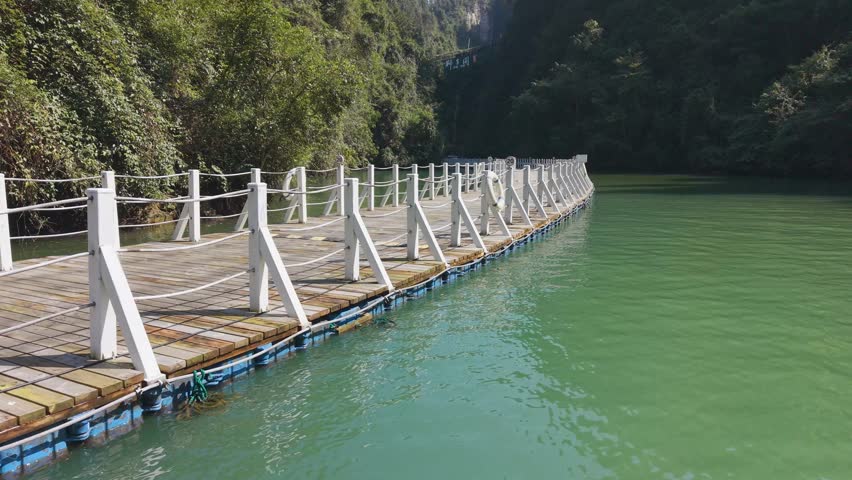Close fly by aerial of the Shiziguan Floating Bridge in Hubei, showing modular HDPE pontoon floats and wooden deck structure on calm river water.