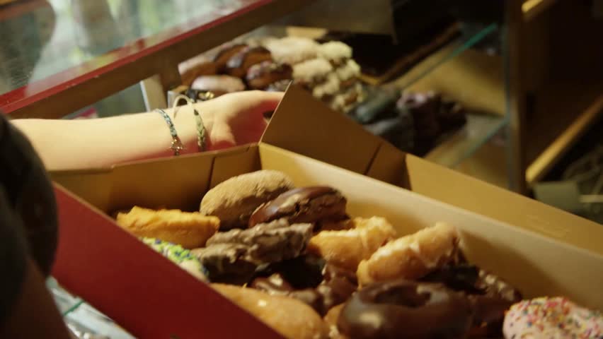 Assorted donuts in box. Close up shot shows donuts of various flavors in a red cardboard box being held by a person. Great for food, pastry, and snack themes.