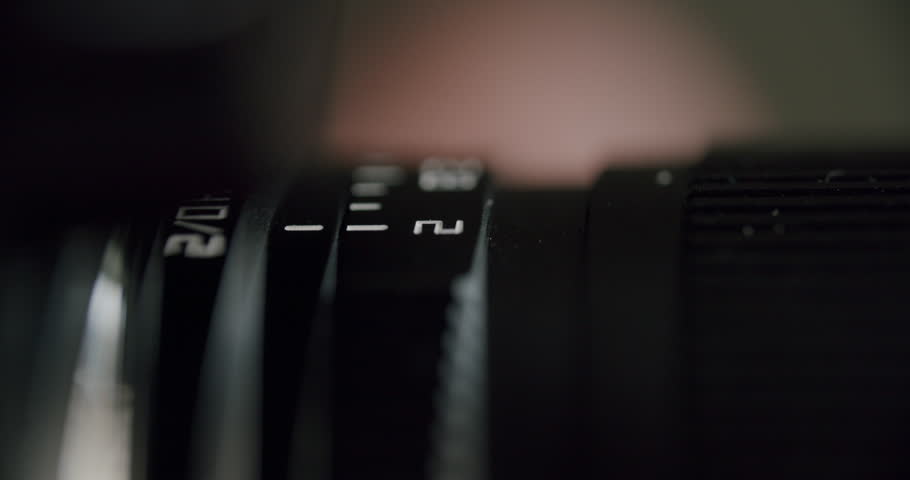 Side-angle close-up of a hand adjusting the aperture ring on a camera lens, with the selected f-stop clearly visible, showing precise manual control and detailed optical markings.