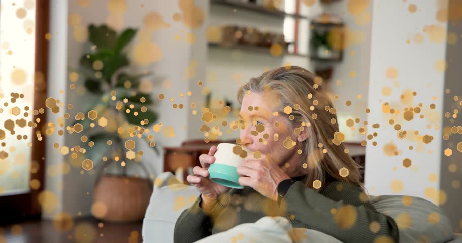 Woman lifting mug, sipping, tucking hair, cradling, smiling while gold bokeh obscuring view for ads. Adult, female, cup, cozy, serenity, relaxation, sofa