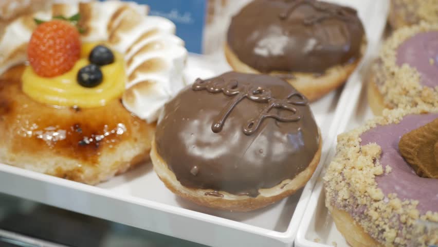 Close up of assorted donuts on a white tray. Includes donuts with chocolate icing, pastry cream, meringue, strawberry and blueberry toppings. Available at the shop.