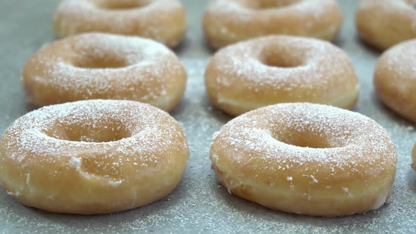 Close up of Rows of glazed donuts covered in white powdered sugar sit on a gray tray. Ready to be enjoyed, these treats look fresh and delicious. donuts on a tray, delicious treats, 4k hd