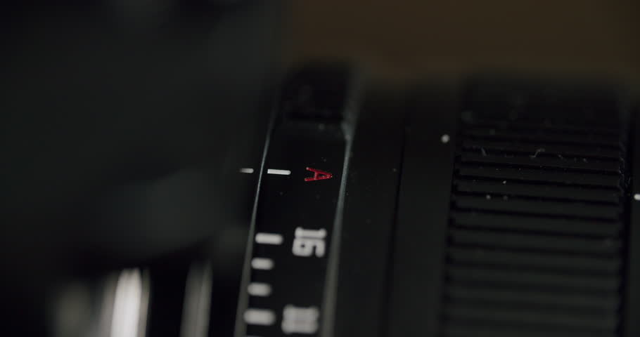 Slightly elevated close-up view of a hand adjusting the aperture ring on a camera lens, with the f-stop number clearly visible, highlighting precise manual control and detailed lens markings.