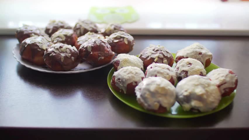 Two plates of homemade donuts are on a dark table. Donuts are covered in chocolate and almond toppings. Some are covered in white icing.