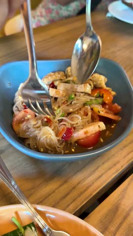 Hands mix spicy glass noodle salad in daylight, vibrant ingredients visible, close-up, natural lighting