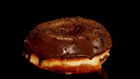 A glazed chocolate donut covered in tiny sprinkles shows condensation droplets. The surface texture is highlighted against a black backdrop, emphasizing details of the pastry. - Powered by Shutterstock - Get 15% off with code: PIKWIZARD15