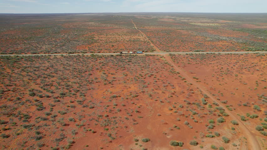 High aerial shot of a roadtrain driving along the Stuart Highway, surrounded by Australia’s deep red desert. The wide open landscape and long straight road highlight the scale of the outback.