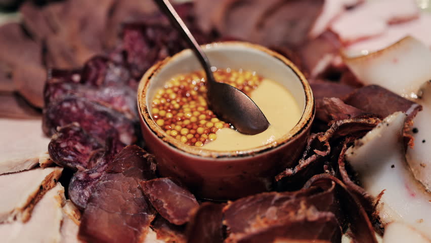 Gourmet charcuterie board with assorted cured meats, smoked slices, and a mustard seed sauce served in a bowl